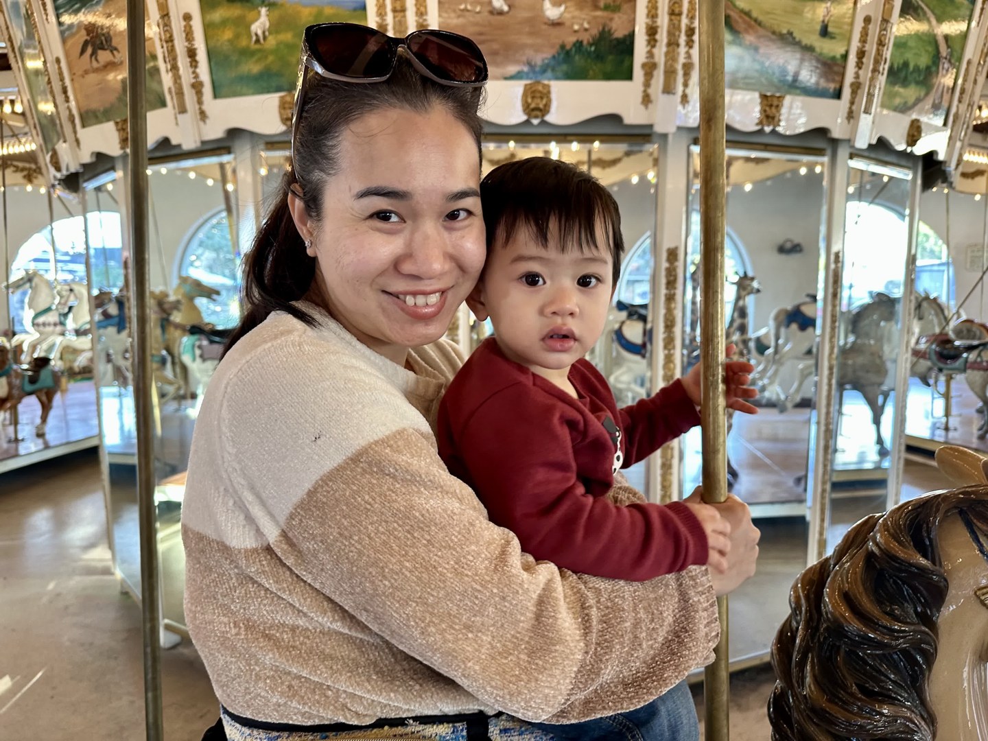 Vy holding Mason on a carousel, facing the camera together.